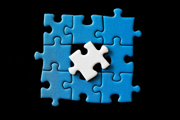 White puzzle piece on top of a blue puzzle on a black background