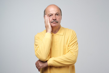 Closeup portrait of mature depressed man in yellow shirt really sad, deep in thought, looking up asking question why me isolated on gray background. Human face expressions, emotion, feeling, reaction