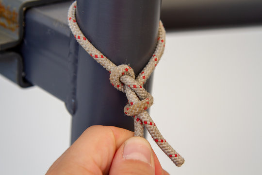 The man ties the textile canvas to the metal stand with the help of a knot of bulls. The Bulin knot. Textile trolley and metal stand.