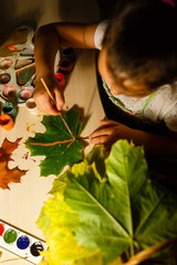 Cute little girl drawing with paint autumn leaves at home