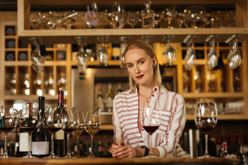 Wine professional. Attractive positive woman smiling to you while standing behind the bar counter