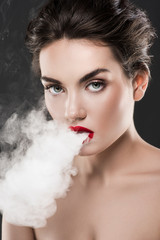stylish naked woman blowing smoke, isolated on grey