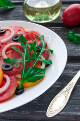 Salad of red and yellow tomatoes with olives, onions and basil. In a white big plate on a wooden background.