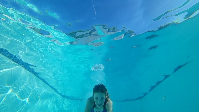 happy smiling girl into bathing suit plunges into water and swims with open eyes in Poolside
