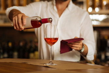 Rose wine. Selective focus of a glass standing on the counter while being filled with wine