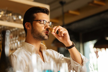 Checking the smell. Pleasant handsome man putting a wine cork to his nose while checking its smell