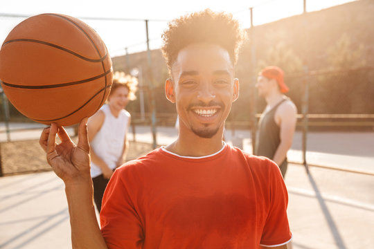 Image of sporty young boy spinning ball on his finger, while playing basketball at the playground outdoor with his team