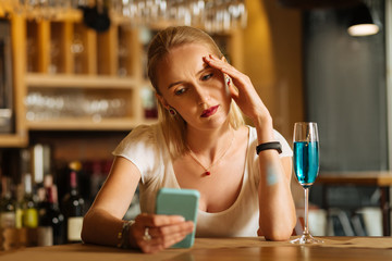 Bad days. Sad depressed woman looking at her smartphone while being in the bad mood
