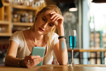 I am lonely. Nice cheerless woman sitting alone in the bar while using her smartphone