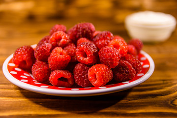 Ceramic plate with ripe raspberries and sour cream on wooden table
