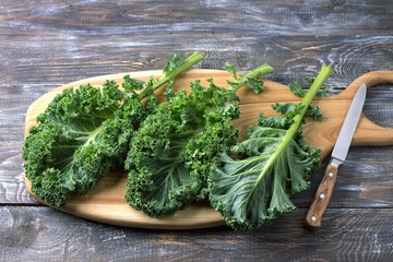 Fresh green curly kale leaves on a cutting board on a wooden table. selective focus. rustic style....