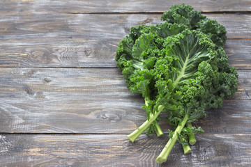 Fresh green curly kale leaves on a cutting board on a wooden table. selective focus. free space. rustic style. healthy vegetarian food - obrazy, fototapety, plakaty