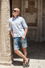 Bald man in sunglasses walking on old narrow street