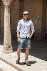 Fototapeta na wymiar Bald man in sunglasses walking on old narrow street