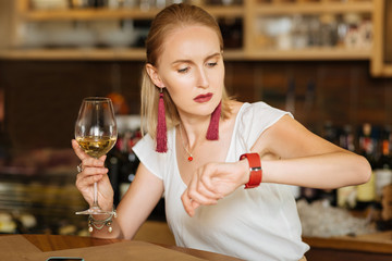 What time is it. Depressed sad woman looking at her watch while waiting for her friend