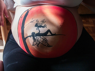 Body art. Painted belly of a pregnant young woman with a fairy drawing