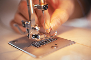 Fototapeta na wymiar Closeup shot of hand of anonymous tailor putting thin thread in needle of modern sewing machine in workshop
