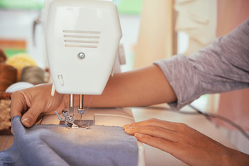 Crop hands of anonymous fashion designer sewing blue apparel on modern sewing machine in studio
