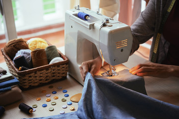From above shot of unrecognizable fashion designer using modern sewing machine to make nice apparel...