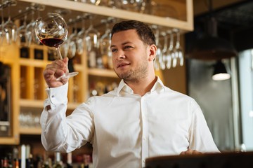 Glass of wine. Joyful nice man holding a glass of wine in front of him while checking the smell