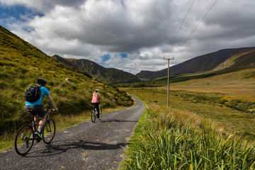 Fototapeta premium Active couple biking on a rural country road in the scenic mountain valley landscape of the Dingle peninsula, County Kerry in the Republic of Ireland