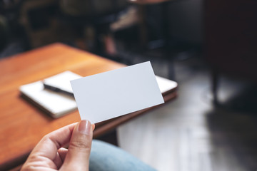A hand holding white empty business card with notebook on wooden table