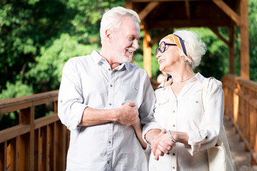 Hand in hand. Elderly bearded man smiling broadly while holding hand of his beaming beautiful wife while walking together