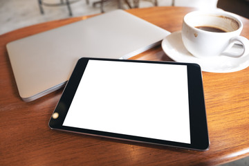 Top view mockup image of a black tablet pc with blank desktop white screen with laptop and coffee cup on wooden table