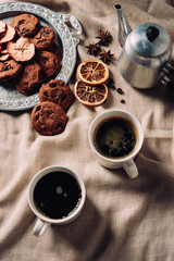 top view of cups of coffee with chocolate chip cookies and vintage metal pot on beige cloth