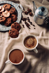 top view of cups of fresh coffee with chocolate chip cookies and vintage metal pot on beige cloth