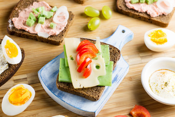 Breakfast table with cheese sandwiches, sausage, vegetables, hard boiled eggs and fruits