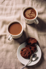top view of cups of coffee with chocolate chip cookies on plate on beige cloth