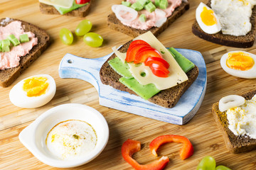 Breakfast table with cheese sandwiches, sausage, vegetables, hard boiled eggs and fruits