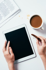 cropped shot of woman using tablet while eating chocolate chip cookie with coffee on white surface