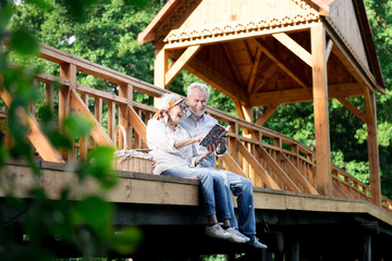 Family photo album. Retired married couple feeling happy while looking at their family photo album sitting on the bridge