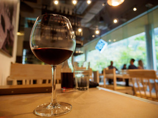 Wide close-up of glass of red wine on wooden table at an Italian restaurant, customers in background. Shallow focus, Bangkok, Thailand. Travel and cuisine concept.