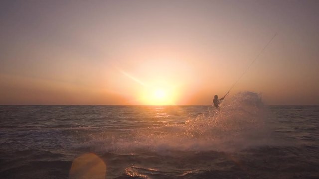 A man is engaged in kitesurfing on the sea during the dawn, slow motion