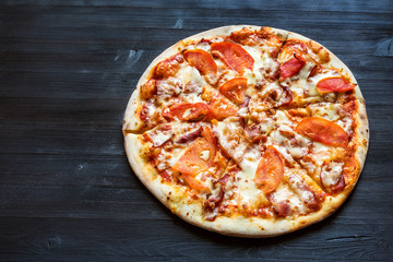 pizza with bacon and tomatoes on dark table