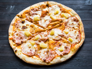 pizza with ham and pineapple on dark wooden board