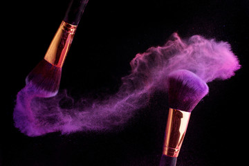 Make-up brush with colorful powder splashes explosion on black background