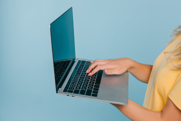 Fototapeta na wymiar cropped image of girl holding laptop with blank screen isolated on blue