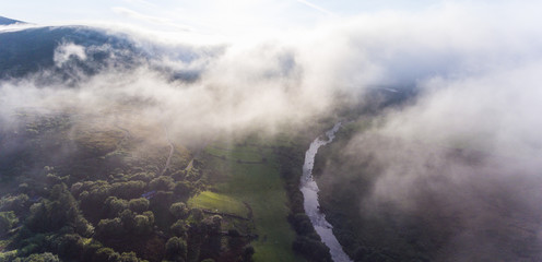 Misty autumn aerial view through rural Irish countryside, view of river and trees through foggy clouds sunlight 