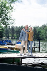 Couple near river. Aged wife and husband wearing bright sunglasses standing near the river and little boats