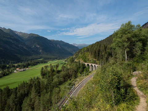 Train and the bridge in Switzerland with green slopes. The Rhaetian Railway section from the Albula/Bernina area (the part from Thusis to Tirano, including St Moritz), August, 2018