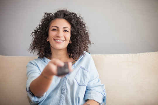 Woman pressing remote control on sofa