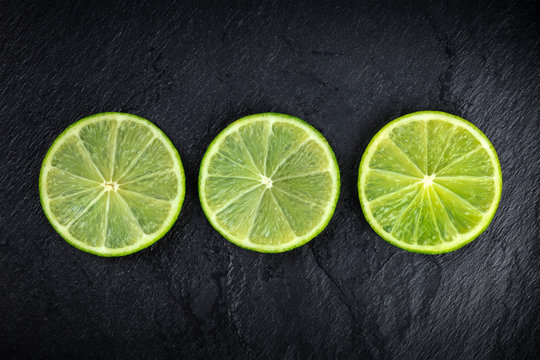 An overhead photo of three lime slices on a black background