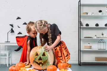 little kids in halloween costumes looking into pumpkin at home