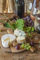 Fototapeta na wymiar Various of french cheeses, nuts, grapes and wine on rustic background,vertical picture