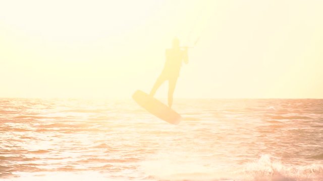 A man is riding a kitesurf and is flying into the air, slow motion
