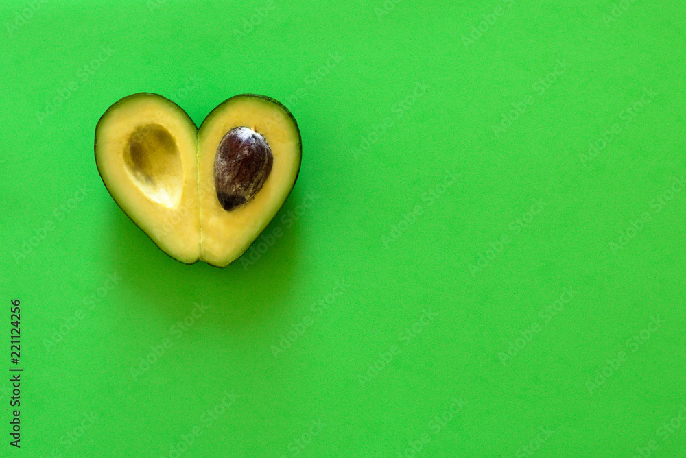 Wall mural Heart-shaped avocado on  green background